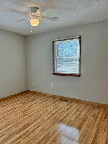 spare room with baseboards, light wood-style floors, visible vents, and a textured ceiling