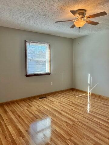 empty room with visible vents, light wood-style floors, a ceiling fan, and a textured ceiling