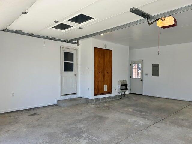 garage featuring heating unit, electric panel, a garage door opener, and baseboards