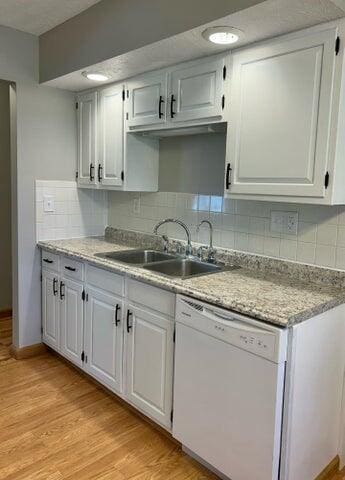 kitchen featuring light wood-style flooring, a sink, backsplash, white cabinets, and dishwasher