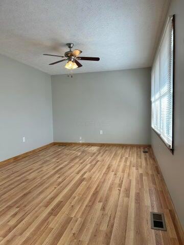 empty room with ceiling fan, light wood-style floors, visible vents, and a textured ceiling