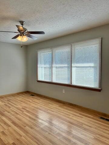 empty room with visible vents, light wood-style floors, a ceiling fan, and a textured ceiling