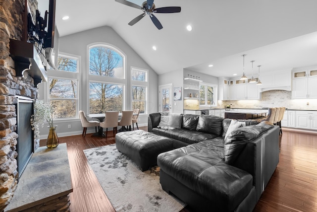 living area with high vaulted ceiling, dark wood-style flooring, a fireplace, a ceiling fan, and baseboards