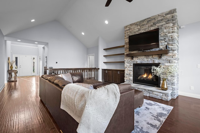 living room featuring baseboards, a ceiling fan, hardwood / wood-style flooring, a stone fireplace, and high vaulted ceiling