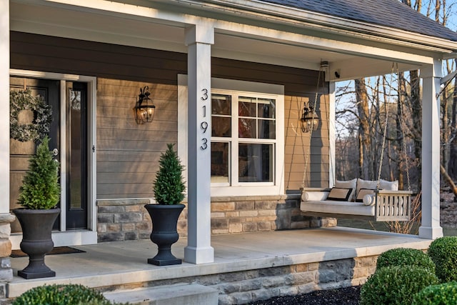 view of exterior entry with a shingled roof, covered porch, and stone siding