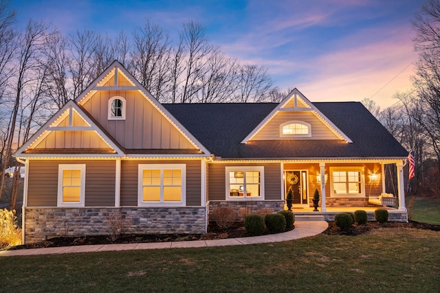 craftsman inspired home with covered porch, stone siding, roof with shingles, a front lawn, and board and batten siding