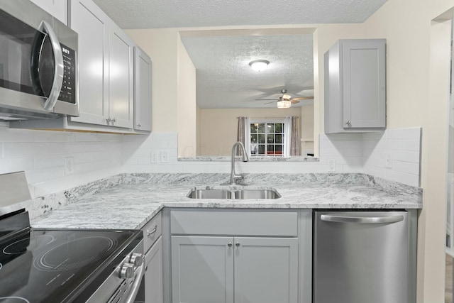 kitchen with sink, gray cabinetry, decorative backsplash, stainless steel appliances, and a textured ceiling