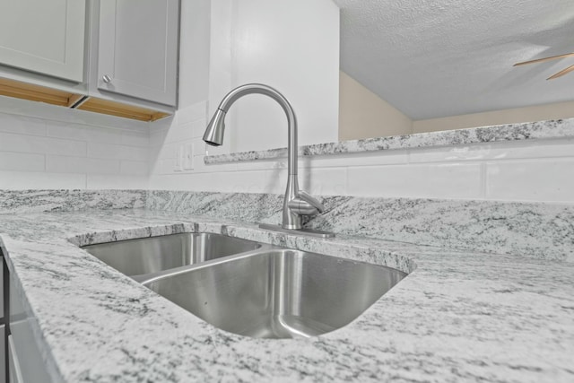 interior details with sink, decorative backsplash, light stone countertops, and ceiling fan