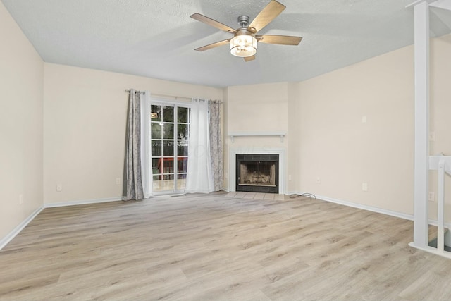 unfurnished living room featuring ceiling fan, a tile fireplace, light hardwood / wood-style flooring, and a textured ceiling