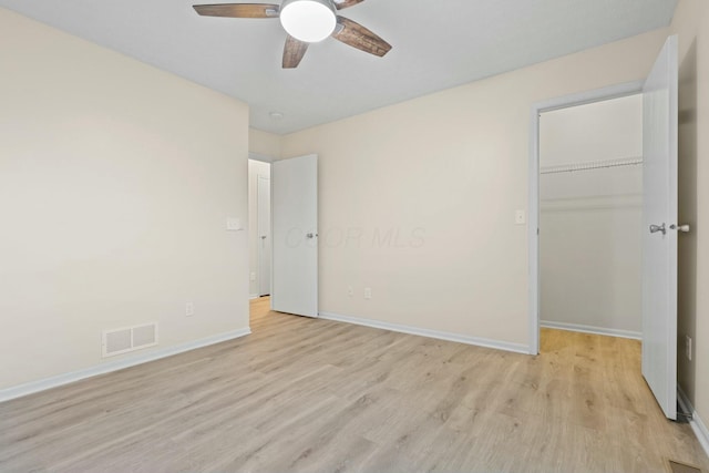 unfurnished bedroom featuring ceiling fan, a spacious closet, light hardwood / wood-style floors, and a closet