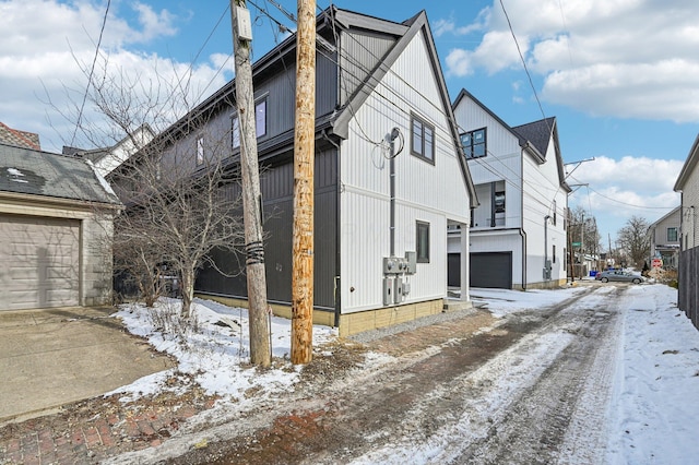 view of snow covered exterior with a residential view, driveway, and an attached garage