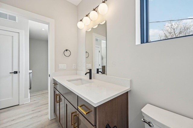 half bathroom featuring toilet, visible vents, wood finished floors, and vanity