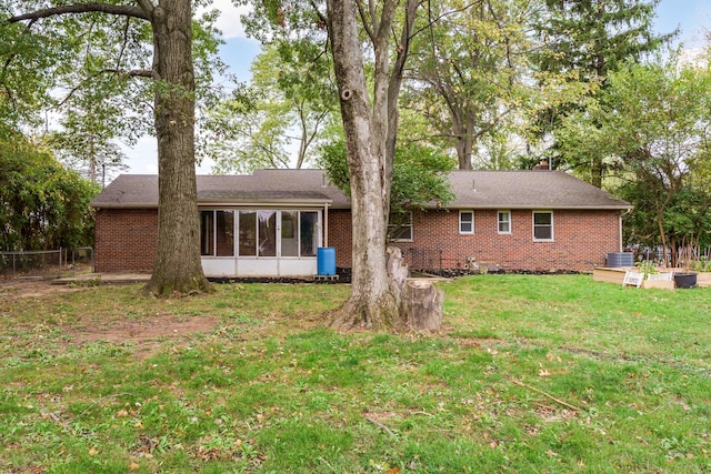 rear view of property with a sunroom, central AC unit, and a lawn