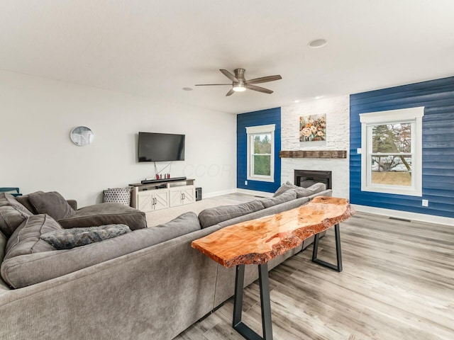 living room featuring light hardwood / wood-style flooring, a stone fireplace, a wealth of natural light, and ceiling fan