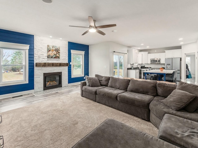 living room with a stone fireplace, light hardwood / wood-style floors, and ceiling fan