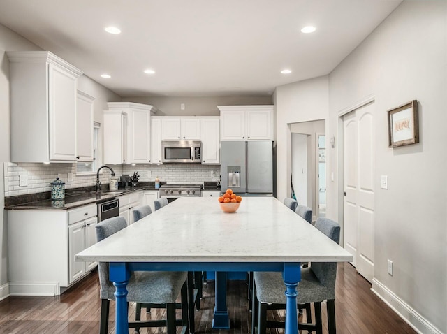 kitchen with appliances with stainless steel finishes, sink, white cabinets, dark stone counters, and a center island