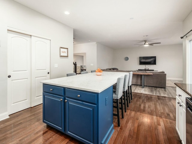 kitchen with blue cabinets, light stone counters, a center island, dark hardwood / wood-style flooring, and a kitchen breakfast bar