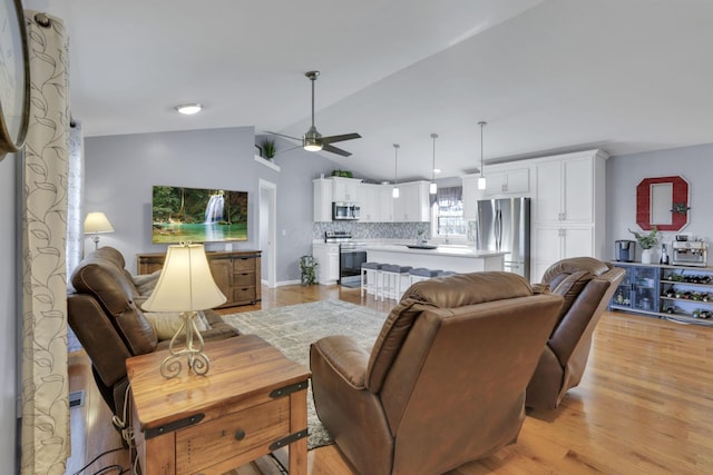 living room with ceiling fan, vaulted ceiling, and light hardwood / wood-style flooring