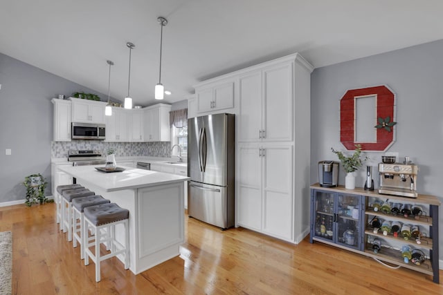 kitchen featuring pendant lighting, appliances with stainless steel finishes, white cabinetry, light hardwood / wood-style floors, and a kitchen bar