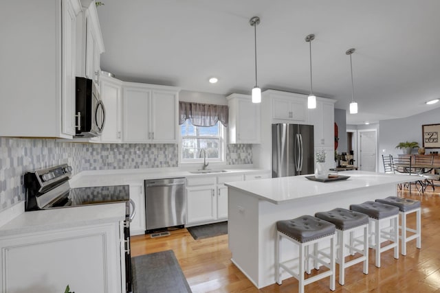 kitchen with sink, hanging light fixtures, stainless steel appliances, a center island, and white cabinets