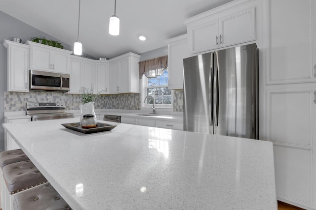 kitchen with sink, white cabinetry, hanging light fixtures, stainless steel appliances, and light stone counters