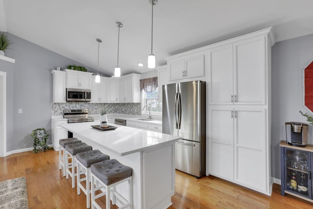 kitchen with white cabinetry, stainless steel appliances, decorative light fixtures, and sink