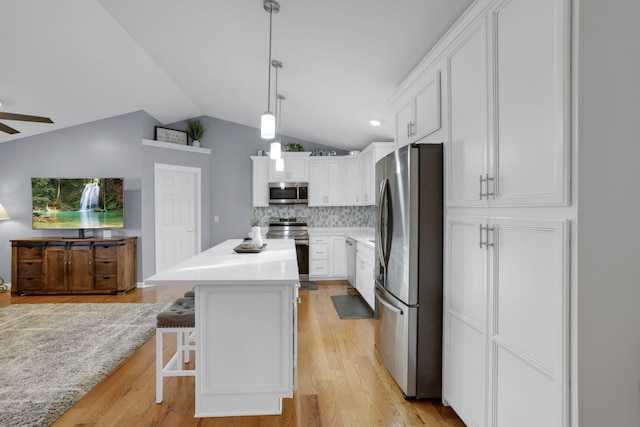 kitchen featuring white cabinetry, a kitchen island, stainless steel appliances, a kitchen bar, and decorative light fixtures