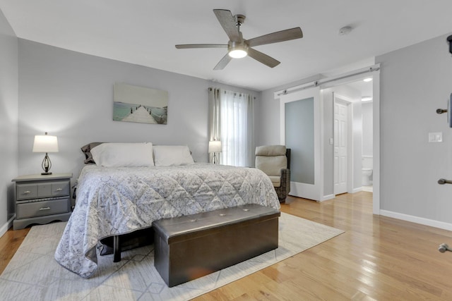 bedroom featuring ceiling fan, ensuite bathroom, a barn door, and light hardwood / wood-style floors