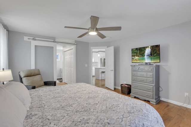 bedroom with ceiling fan, wood-type flooring, and a barn door