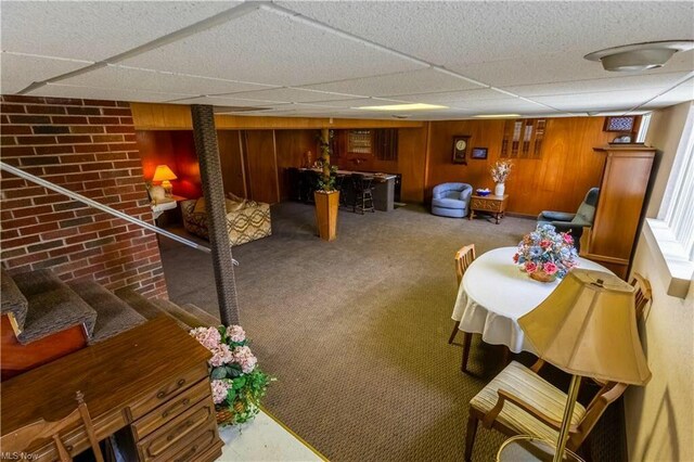 interior space with a drop ceiling, wooden walls, and carpet