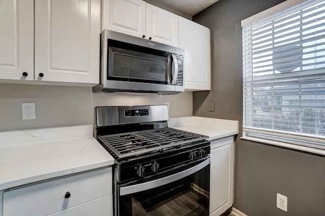 kitchen featuring gas range, white cabinets, and light stone counters