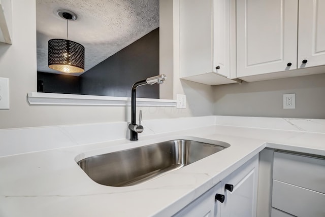 kitchen with sink, pendant lighting, white cabinets, and light stone counters