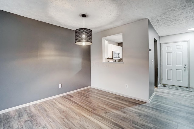 unfurnished dining area featuring a textured ceiling and light wood-type flooring