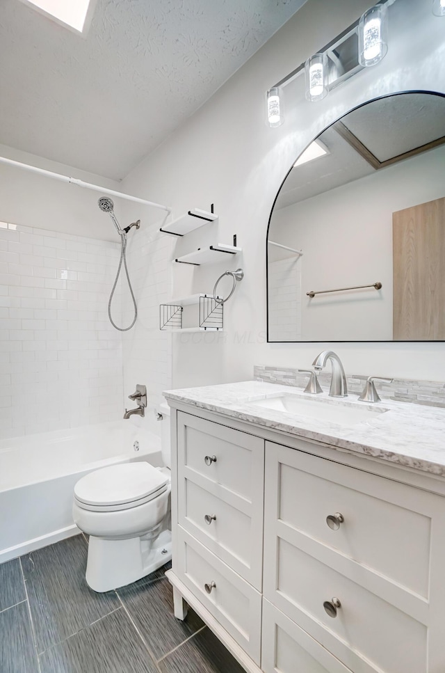 full bathroom with tiled shower / bath combo, vanity, a textured ceiling, and toilet