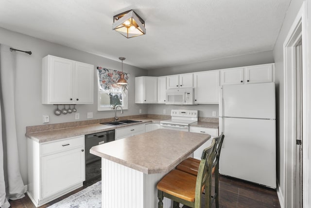 kitchen featuring white appliances, a sink, light countertops, a center island, and decorative light fixtures