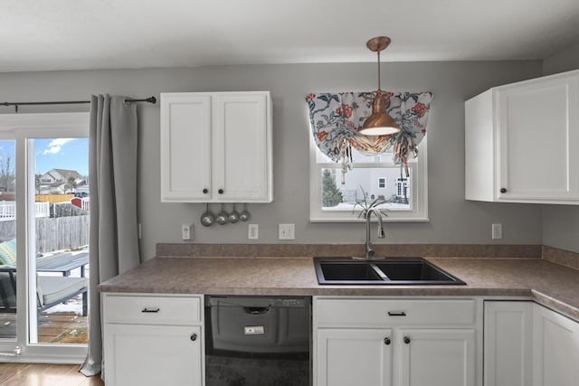 kitchen featuring pendant lighting, black dishwasher, dark countertops, white cabinets, and a sink