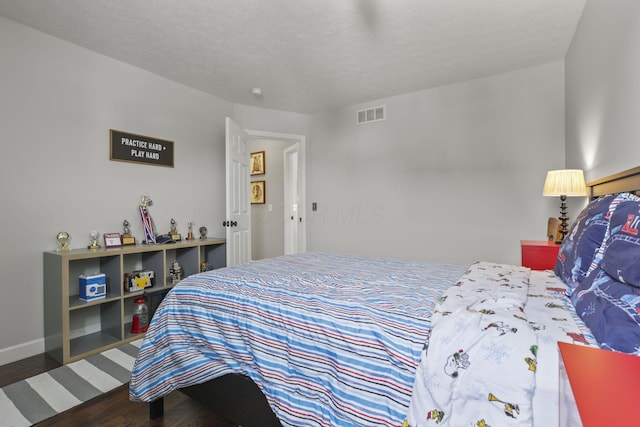 bedroom featuring dark wood-style floors, baseboards, visible vents, and a textured ceiling