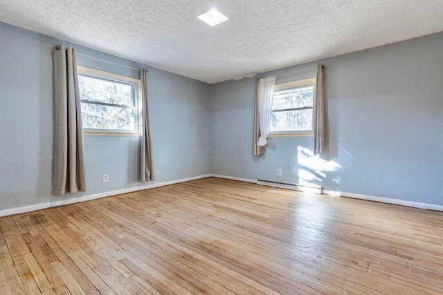 empty room featuring baseboard heating, light hardwood / wood-style flooring, and a wealth of natural light