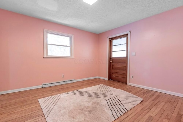 spare room featuring baseboard heating, a textured ceiling, and light wood-type flooring