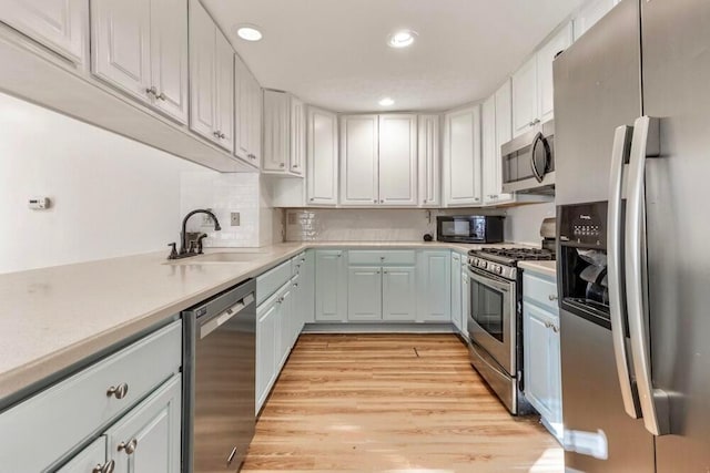 kitchen featuring sink, backsplash, white cabinets, stainless steel appliances, and light wood-type flooring