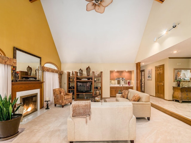 living area with high vaulted ceiling, a fireplace with flush hearth, rail lighting, and light colored carpet