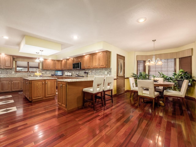 kitchen with a center island, hanging light fixtures, brown cabinets, stainless steel microwave, and dark wood finished floors