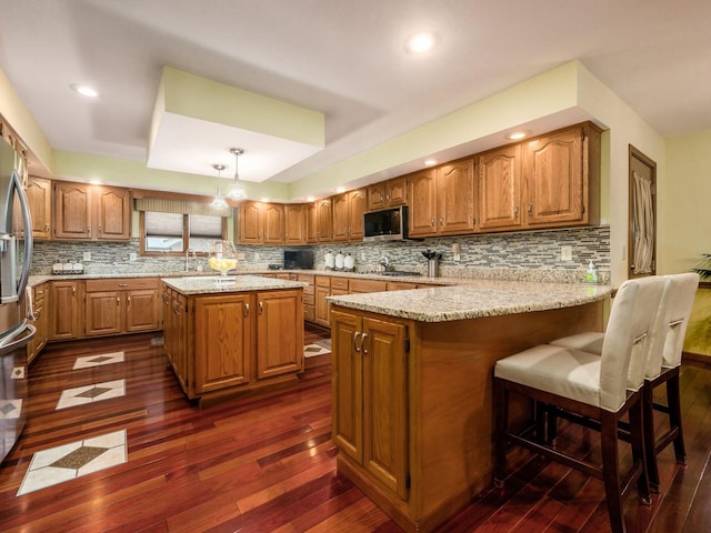 kitchen featuring a peninsula, brown cabinets, stainless steel microwave, and pendant lighting