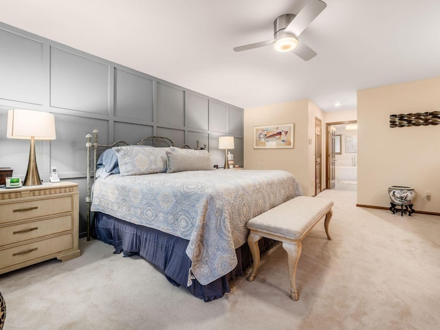 bedroom featuring a ceiling fan, light colored carpet, a decorative wall, and ensuite bathroom