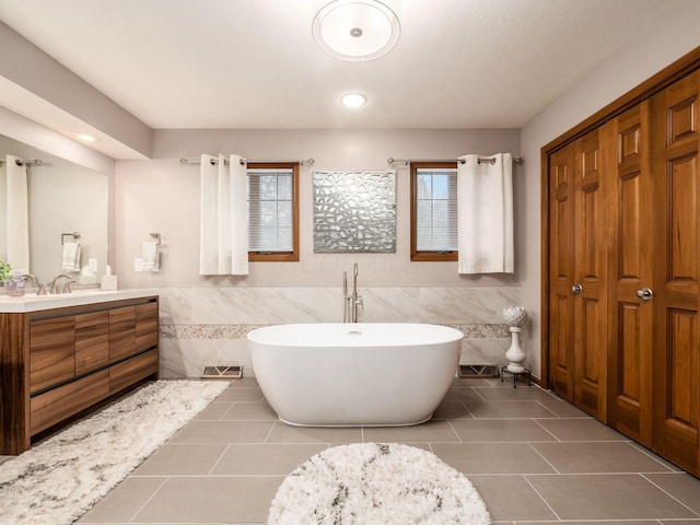 bathroom with a closet, a freestanding bath, tile walls, and vanity