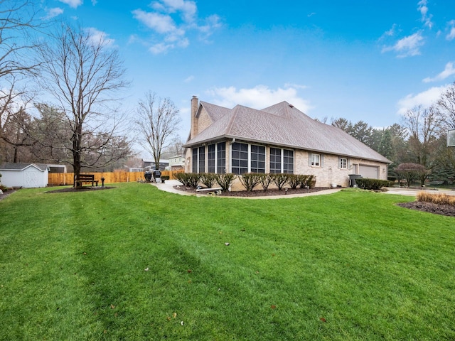 view of side of property with an attached garage, a sunroom, a chimney, and a lawn