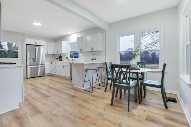 kitchen with tasteful backsplash, white cabinets, a kitchen bar, stainless steel fridge with ice dispenser, and light hardwood / wood-style flooring