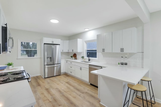 kitchen featuring sink, a breakfast bar area, white cabinetry, appliances with stainless steel finishes, and kitchen peninsula