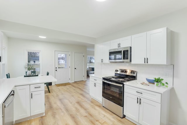 kitchen featuring stainless steel appliances, light wood-type flooring, white cabinets, and backsplash