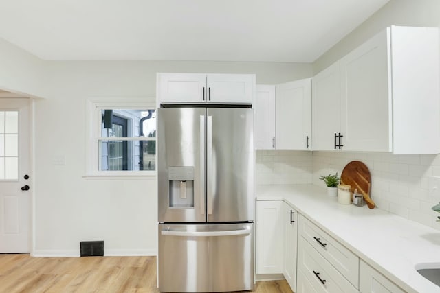 kitchen with stainless steel fridge with ice dispenser, decorative backsplash, plenty of natural light, and white cabinets